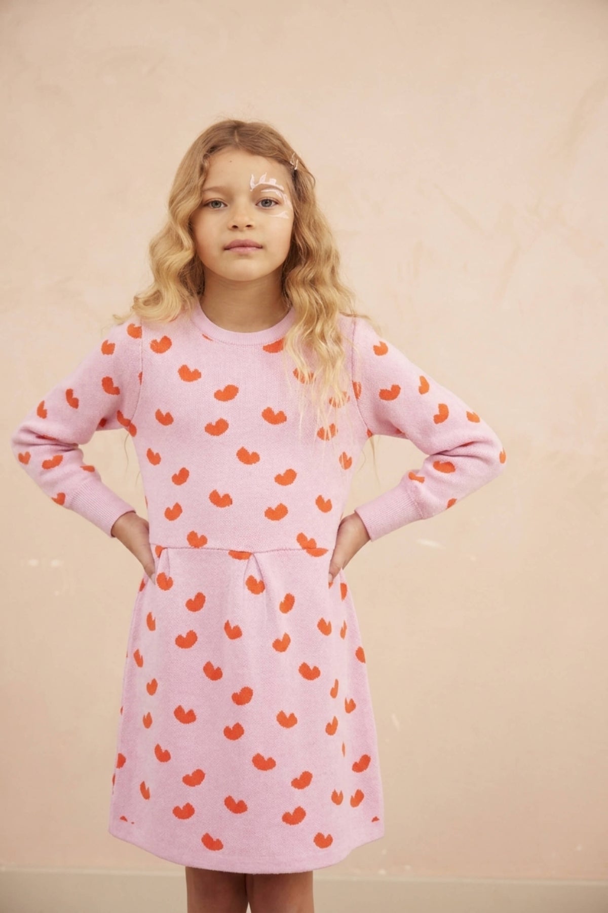 Girl wearing the Love Hearts Dress in bubble gum pink with a pleated skirt