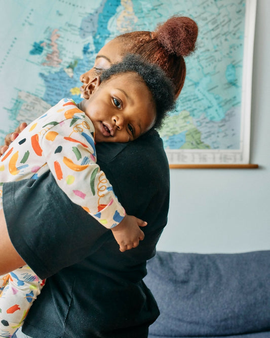 Mother holding baby close in organic cotton sleepsuit - PFAS chemicals in children's clothing what UK parents need to know | Kiddykind