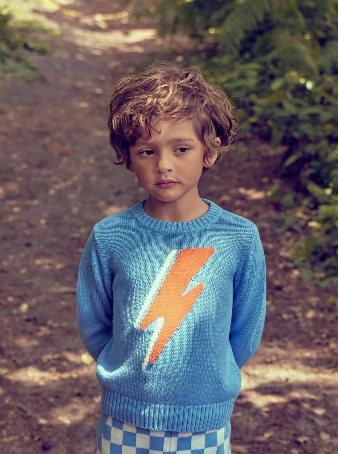 Boy in organic cotton jumper walking along a sunlit forest path - complete guide to buying sustainable baby and kids clothing UK | Kiddykind
