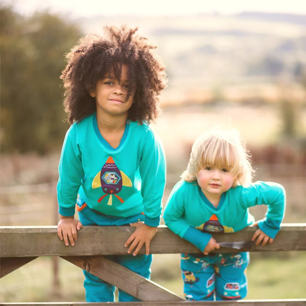 Child in turquoise rocket print organic cotton top outdoors - colourful sustainable kids summer clothes UK | Kiddykind