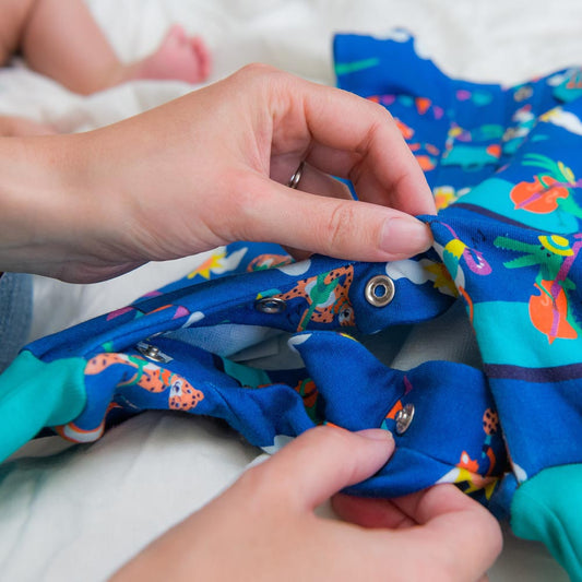 Lady holding organic cotton sleepsuit with baby's feet visible on bed - Plastic Free July reducing plastic for children UK | Kiddykind