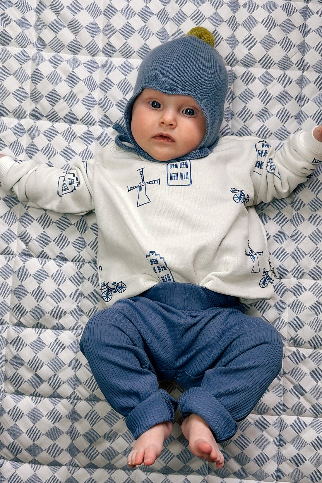 Baby dressed in soft organic cotton outfit lying on white blanket - is polyester safe for babies and their sensitive skin UK | Kiddykind