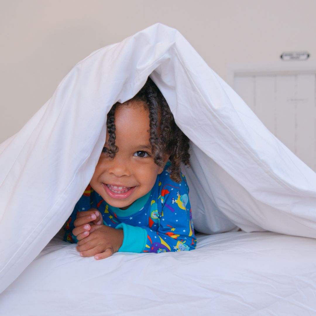 Child peeking from under organic cotton duvet in space print pyjamas - why organic kids pyjamas are the bedtime upgrade parents need UK | Kiddykind