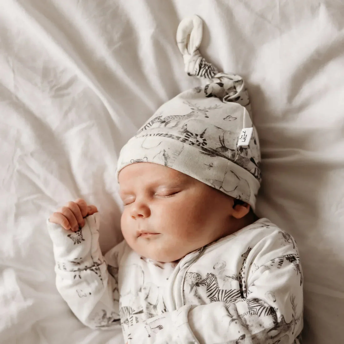 Newborn baby sleeping in organic cotton animal print hat and sleepsuit - UK parent's guide to low-tox baby products | Kiddykind