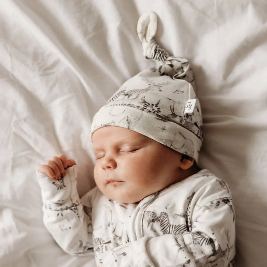 Newborn baby sleeping in organic cotton sleepsuit with animal print hat - best sustainable and organic new baby gift ideas UK | Kiddykind