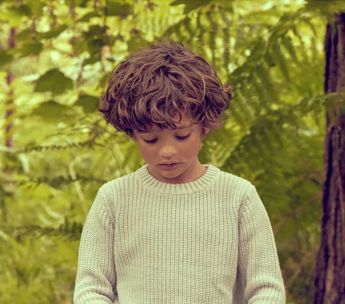 Child in grey organic waffle jumper exploring autumn leaves outdoors - 20 ideas to get kids outside this autumn UK | Kiddykind