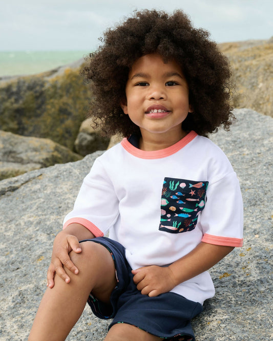 Boy sitting on rock wearing organic cotton t-shirt from Playtime Prints - spend with purpose and raise a kinder future UK | Kiddykind