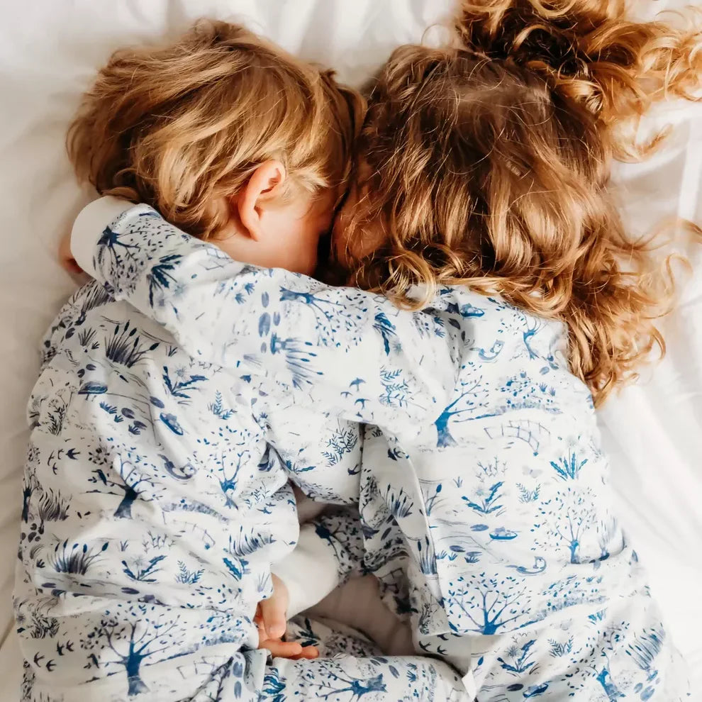 Two toddlers cuddling in a bed with white bedding wearing blue snd white matching organic pyjamas for toddlers