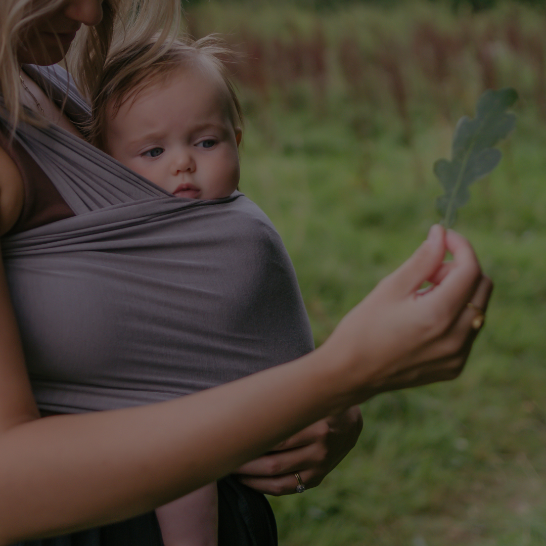 Parent carrying baby in a bamboo and organic cotton baby wrap sling outdoors