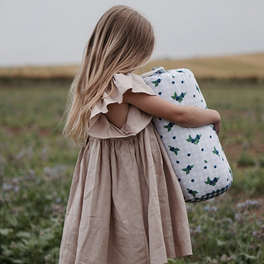 A young girl holding an organic quilt with blueberry and gingham design Evie & Skye