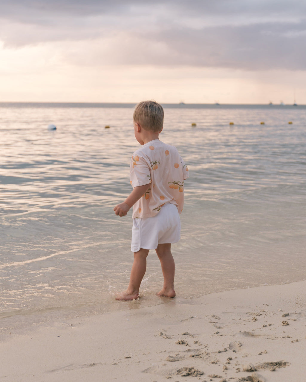 Toddler on the beach at sunset wearing Wildgreen’s Apricot T-shirt from the Island Life collection. Made from 100% GOTS-certified organic cotton, this gender-neutral kids tee features a soft apricot-hued print, perfect for eco-conscious families seeking sustainable and stylish clothing. #OrganicKidswear #SustainableFashion