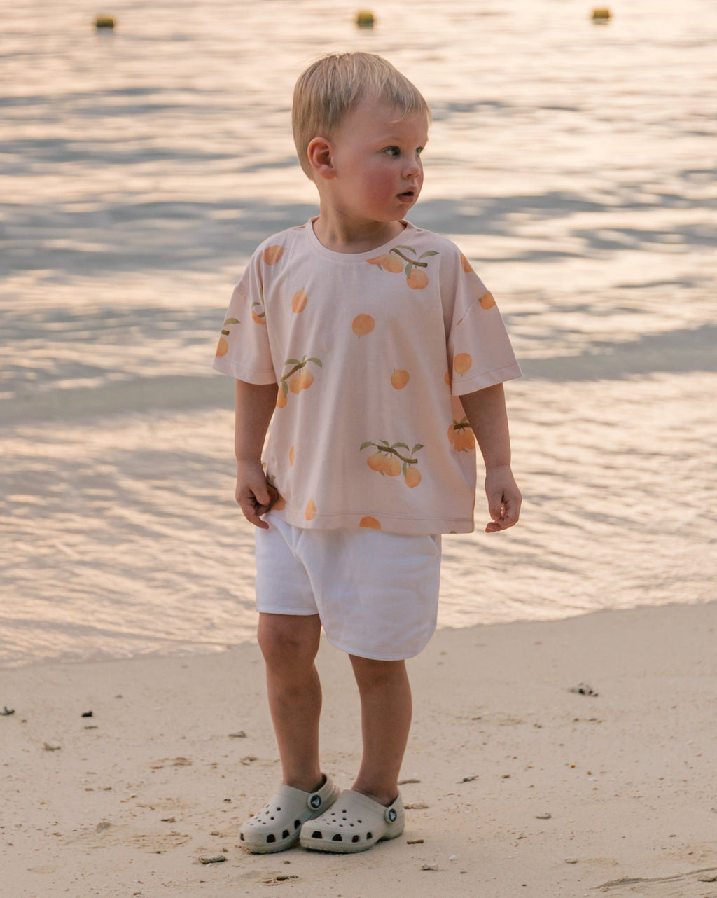 Child on the beach at sunset wearing Wildgreen’s Apricot T-shirt from the Island Life collection. Made from 100% GOTS-certified organic cotton, this unisex kids tee features a soft apricot-hued print, perfect for eco-conscious families seeking sustainable and stylish clothing. #OrganicKidswear #SustainableFashion