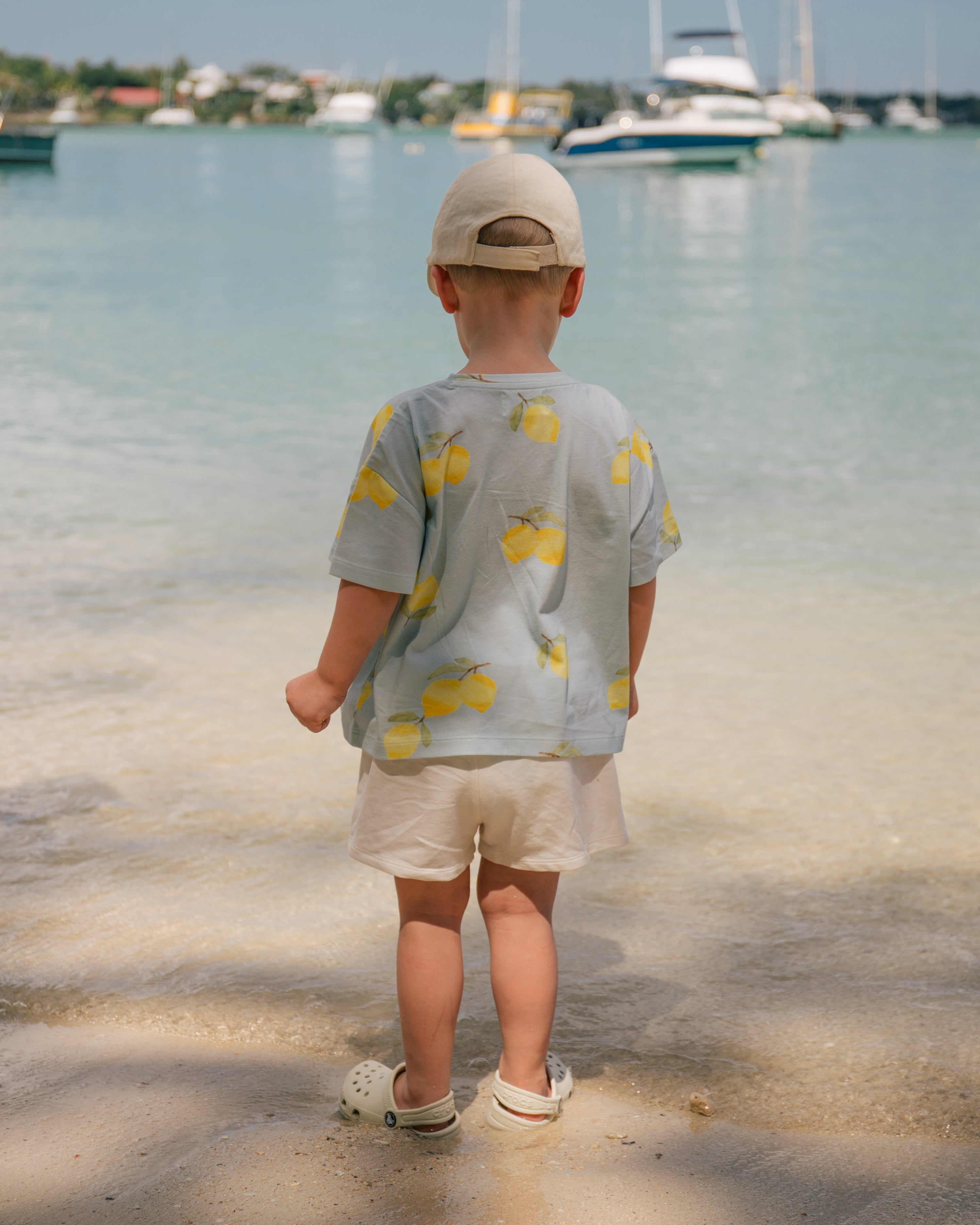 Toddler wearing a Wildgreen Lemon T-shirt from the Island Life collection. Made from 100% GOTS-certified organic cotton, this gender-neutral kids tee features a zesty lemon print, perfect for eco-conscious families who value sustainable fashion. #OrganicKidsClothing #SustainableKidswear