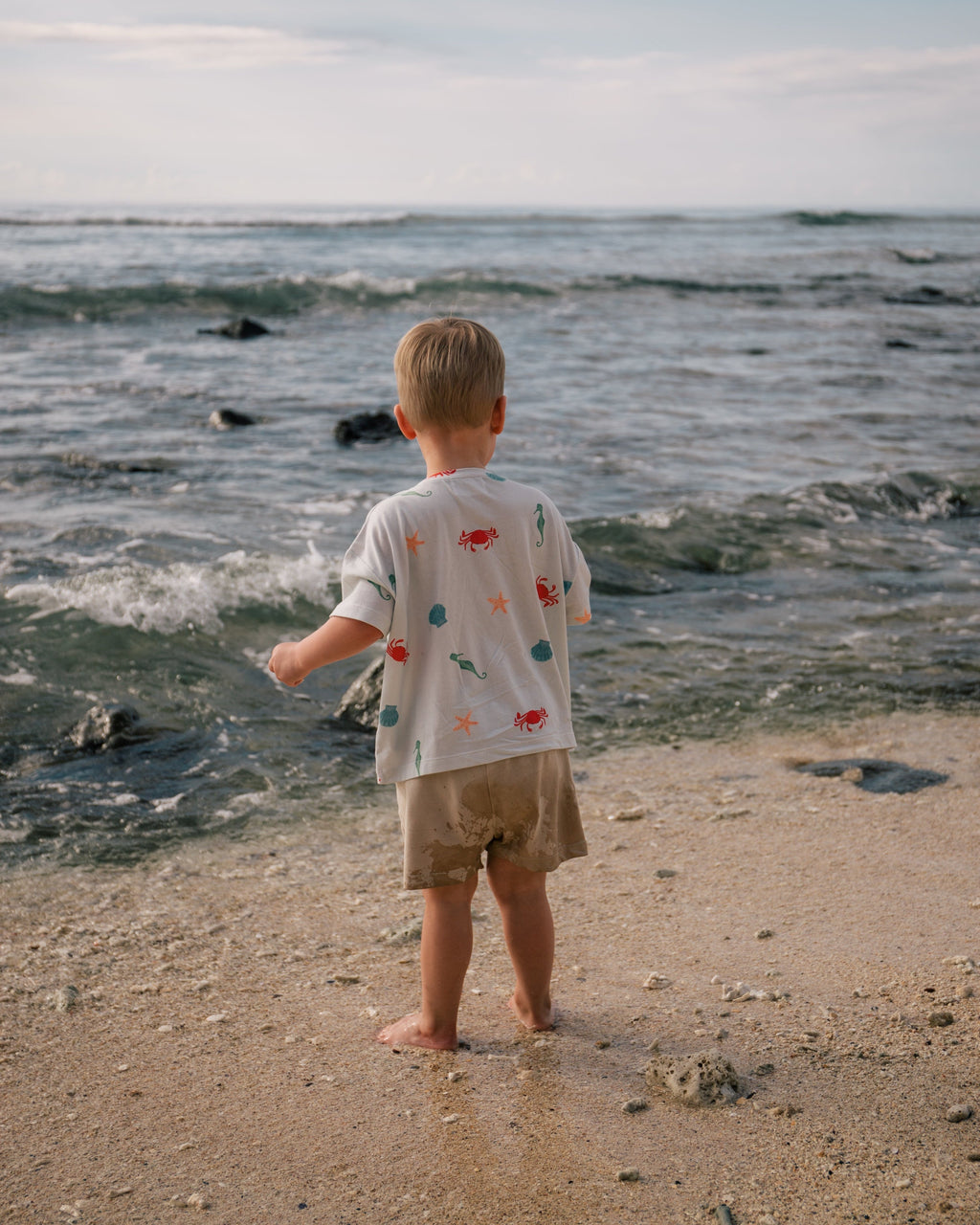 Child on a tropical beach wearing an organic Marine T-shirt from Wildgreen’s Island Life collection. Ethically made from 100% GOTS-certified organic cotton, this unisex kids tee features a vibrant ocean-inspired print. Perfect for eco-conscious families seeking stylish and comfortable clothing