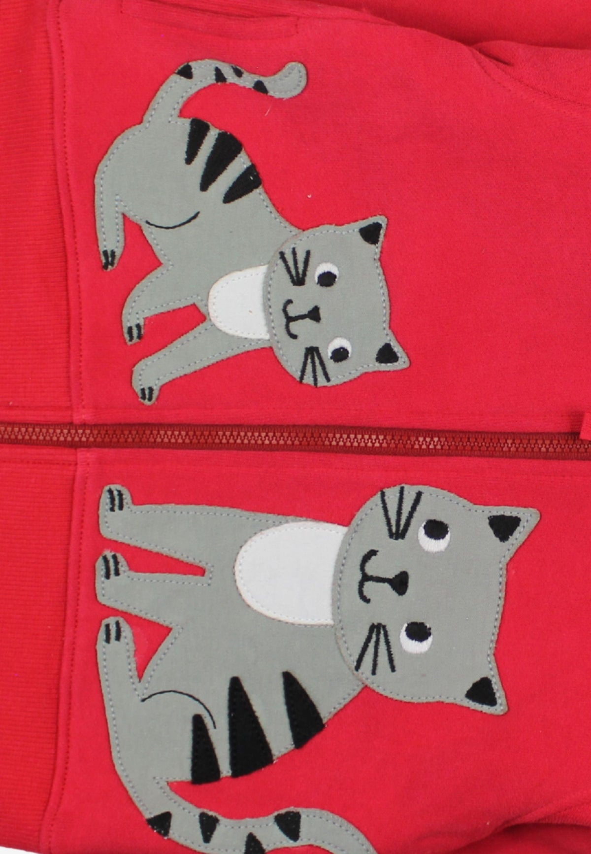 Close-up of a red zippered garment featuring two gray cat appliqués with black stripes and white bellies, separated by a horizontal zipper.
