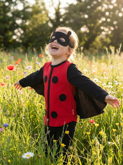 Child in a ladybug costume and mask standing in a field of flowers