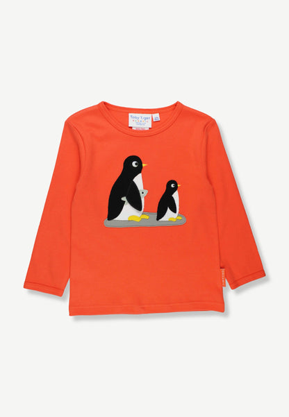A bright orange long-sleeve children's top featuring a graphic of two penguins on the chest, displayed flat against a light off-white background.