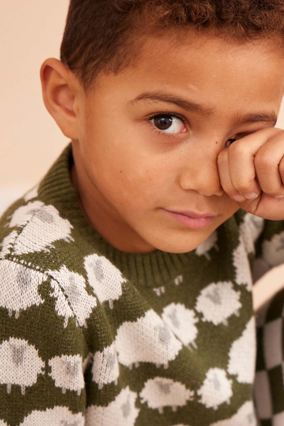 Boy wearing the Flock of Sheep Jumper in avocado green with the sheep pattern across the sleeves