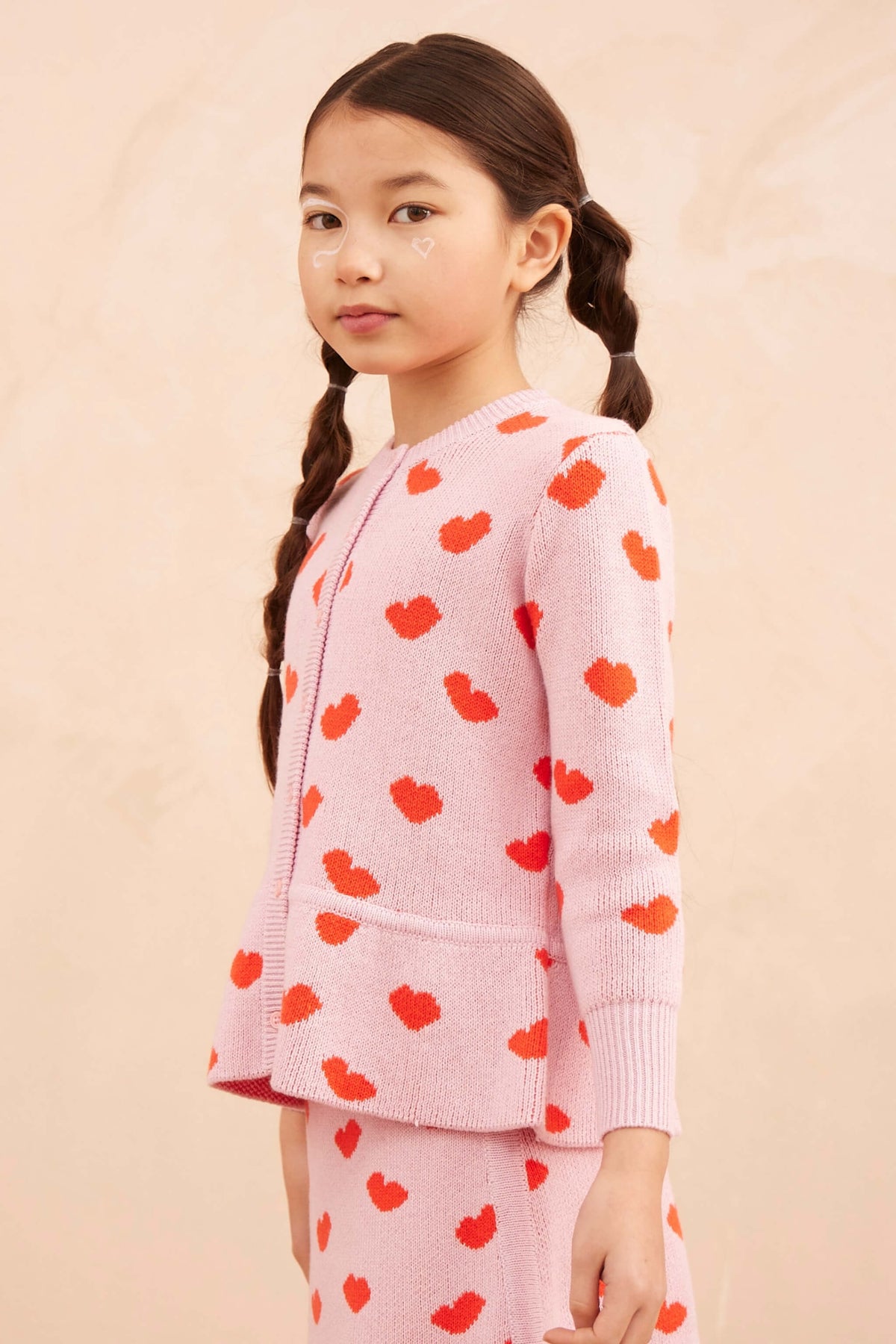 Side view of a girl wearing the Love Hearts Peplum Cardigan in bubble gum pink