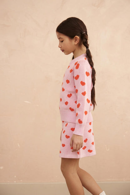 Girl standing in the Love Hearts jumper and skirt set in bubble gum pink
