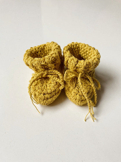 Image shows a pair of saffron yellow organic cotton baby booties.