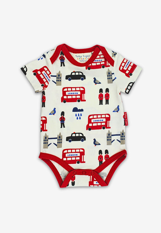 Baby onesie with London-themed print featuring red buses, black cars, and British flags on a white background.