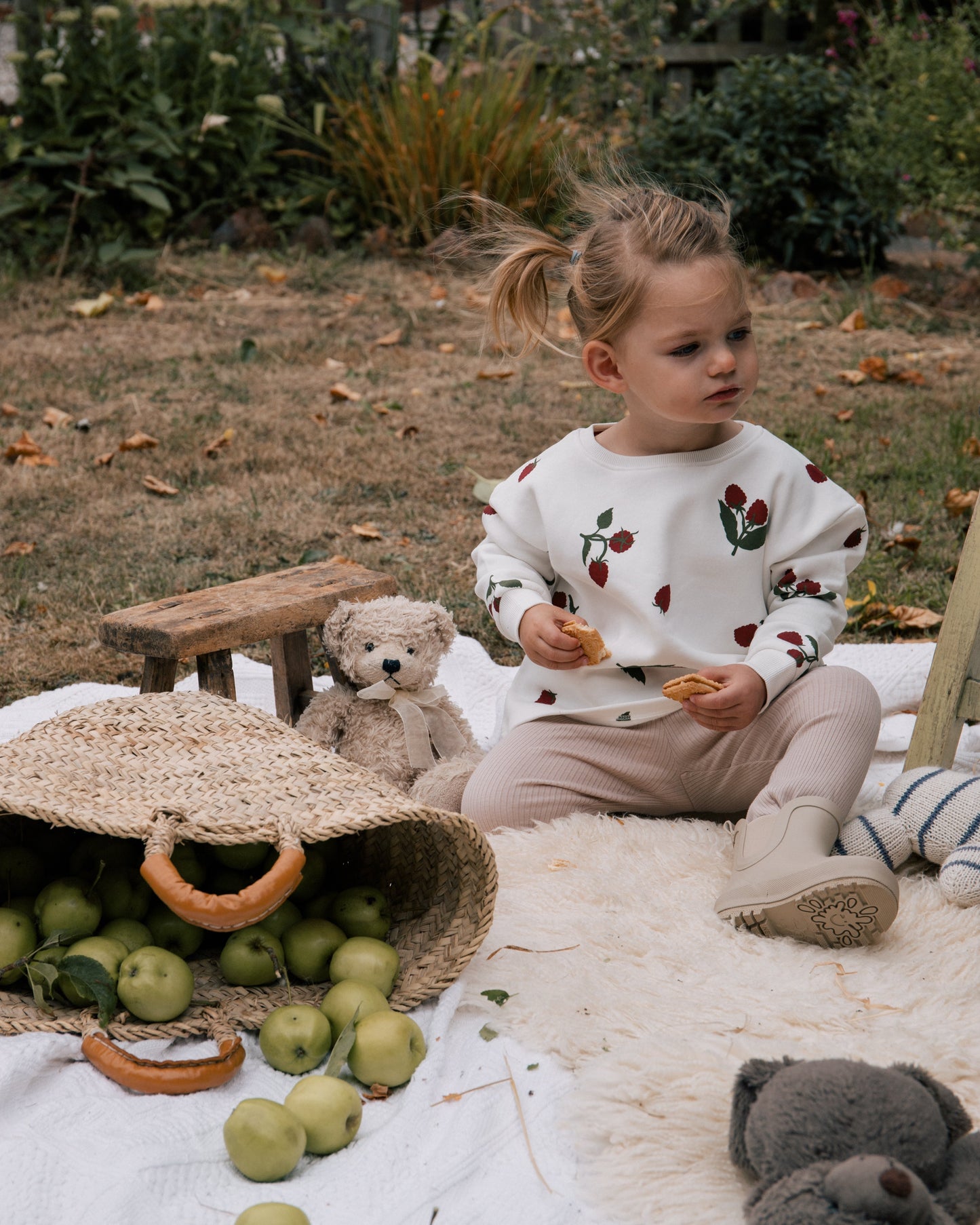 Girl wearing Wildgreen raspberry print sweater made from 100% organic cotton, unisex and gender-neutral sustainable kidswear, having a picnic