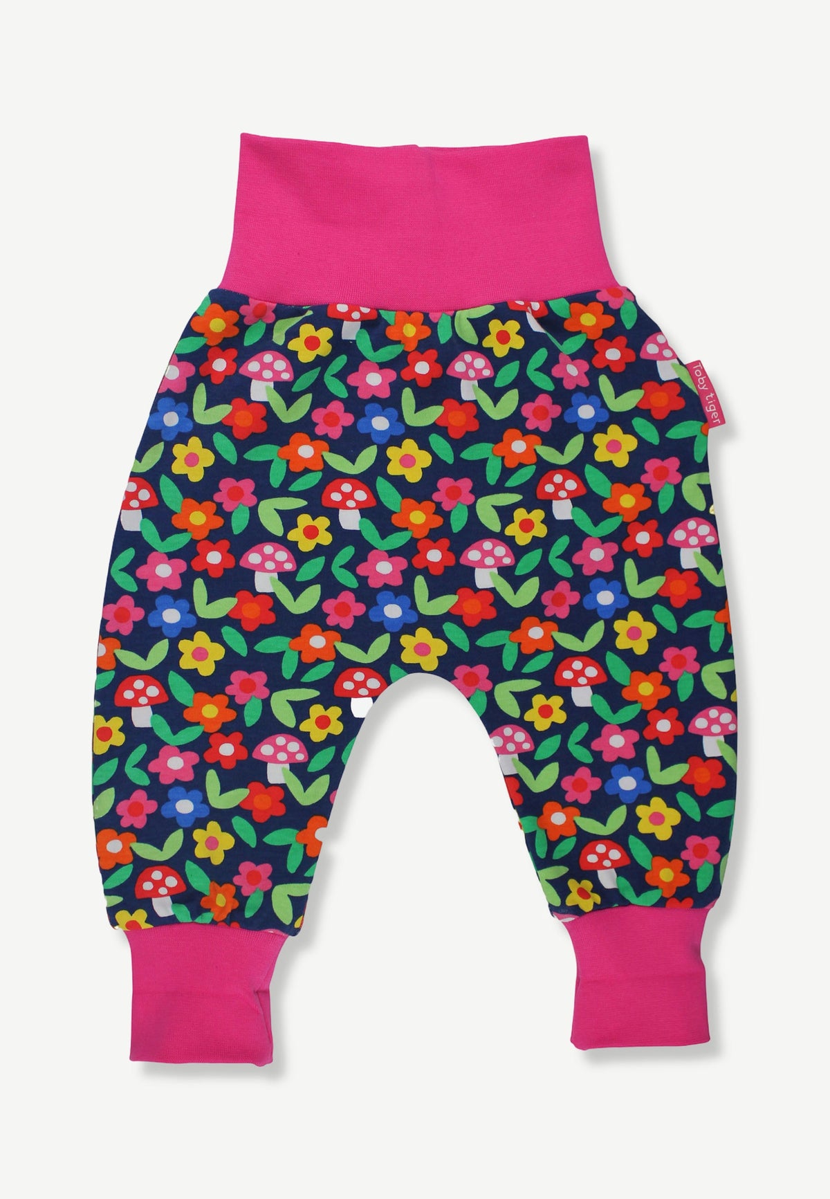 A pair of baby jogger pants featuring a colorful floral and mushroom print on a navy blue background, with bright pink elastic waistband and leg cuffs.