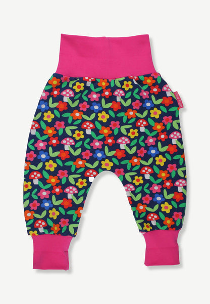A pair of baby jogger pants featuring a colorful floral and mushroom print on a navy blue background, with bright pink elastic waistband and leg cuffs.