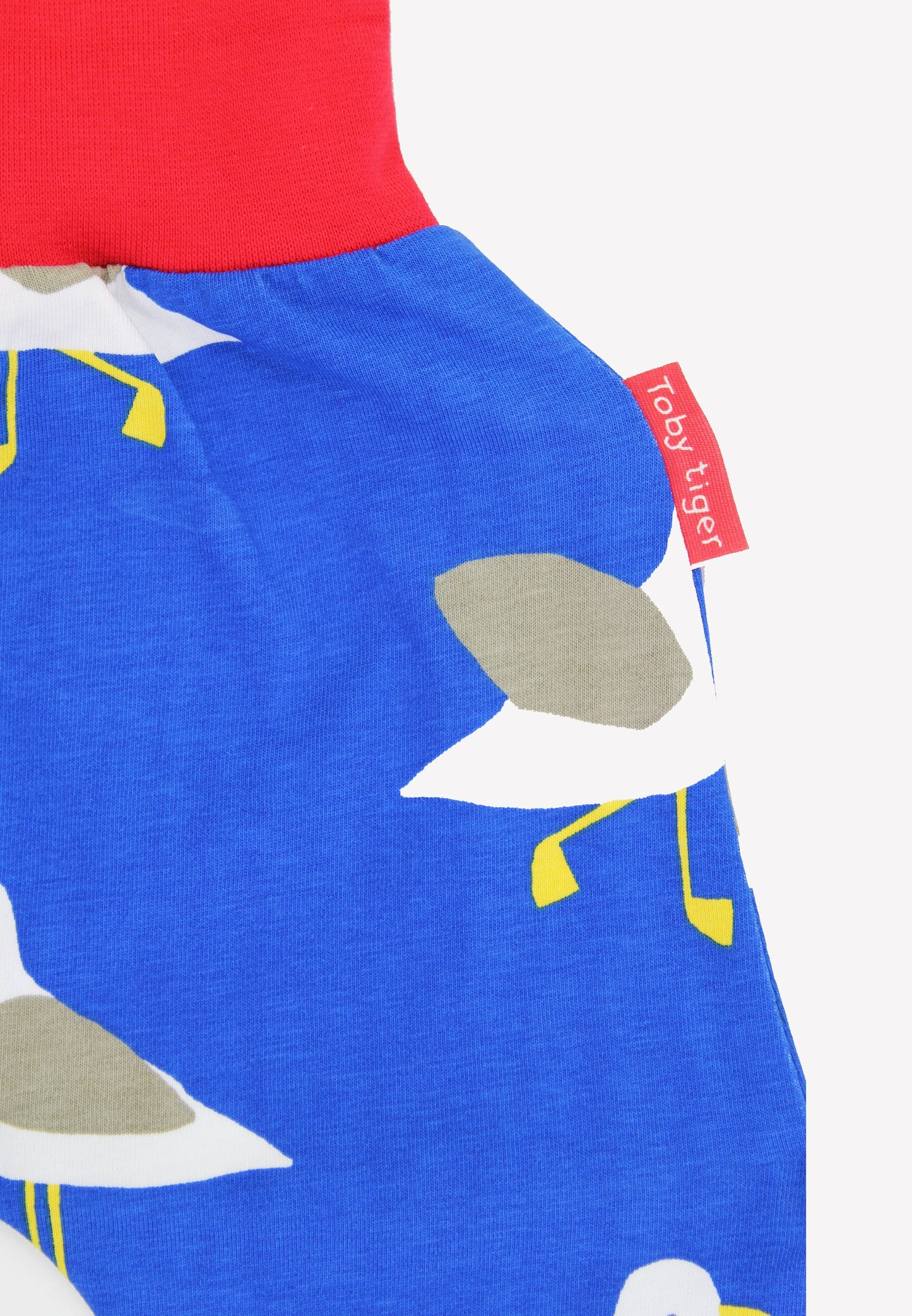 Close-up of a blue garment with bird pattern and red label, featuring the brand 'Toby Tiger'.