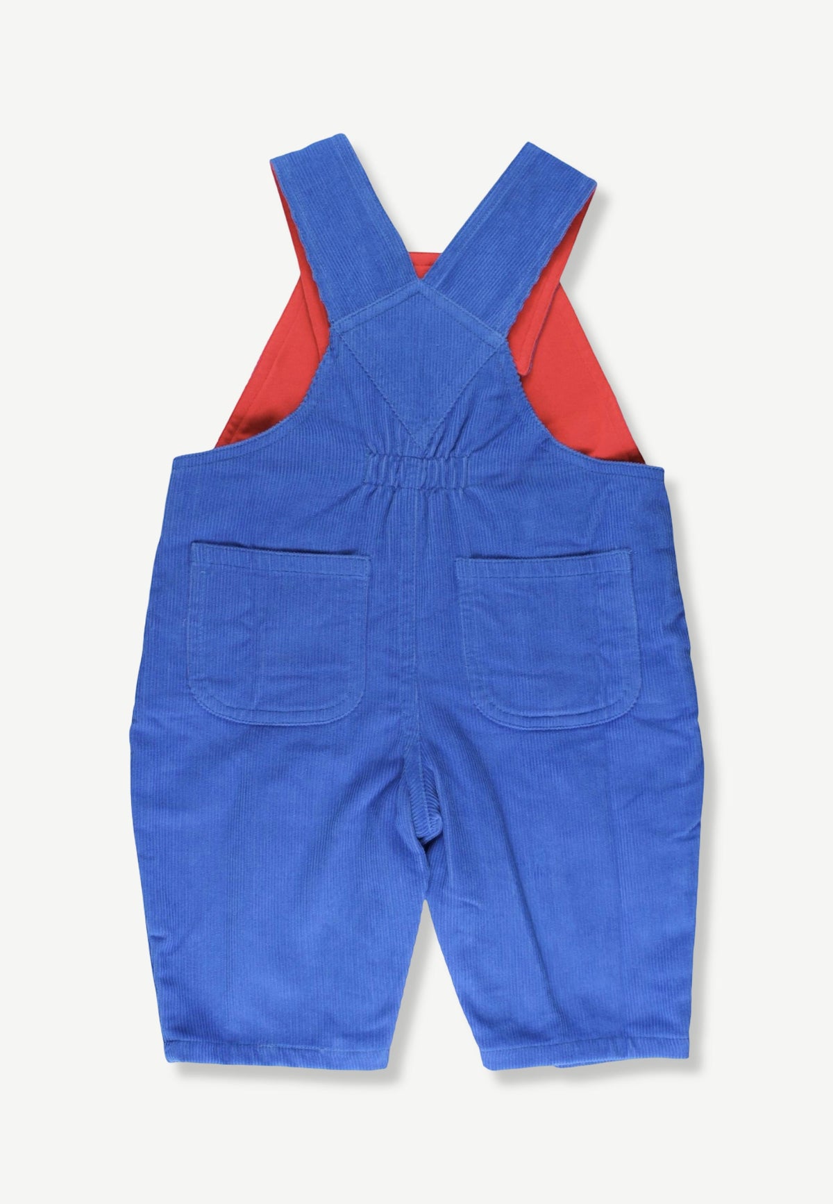 A pair of blue corduroy baby overalls shown from the back, featuring a red inner lining and two front patch pockets, laid flat on a light cream background.
