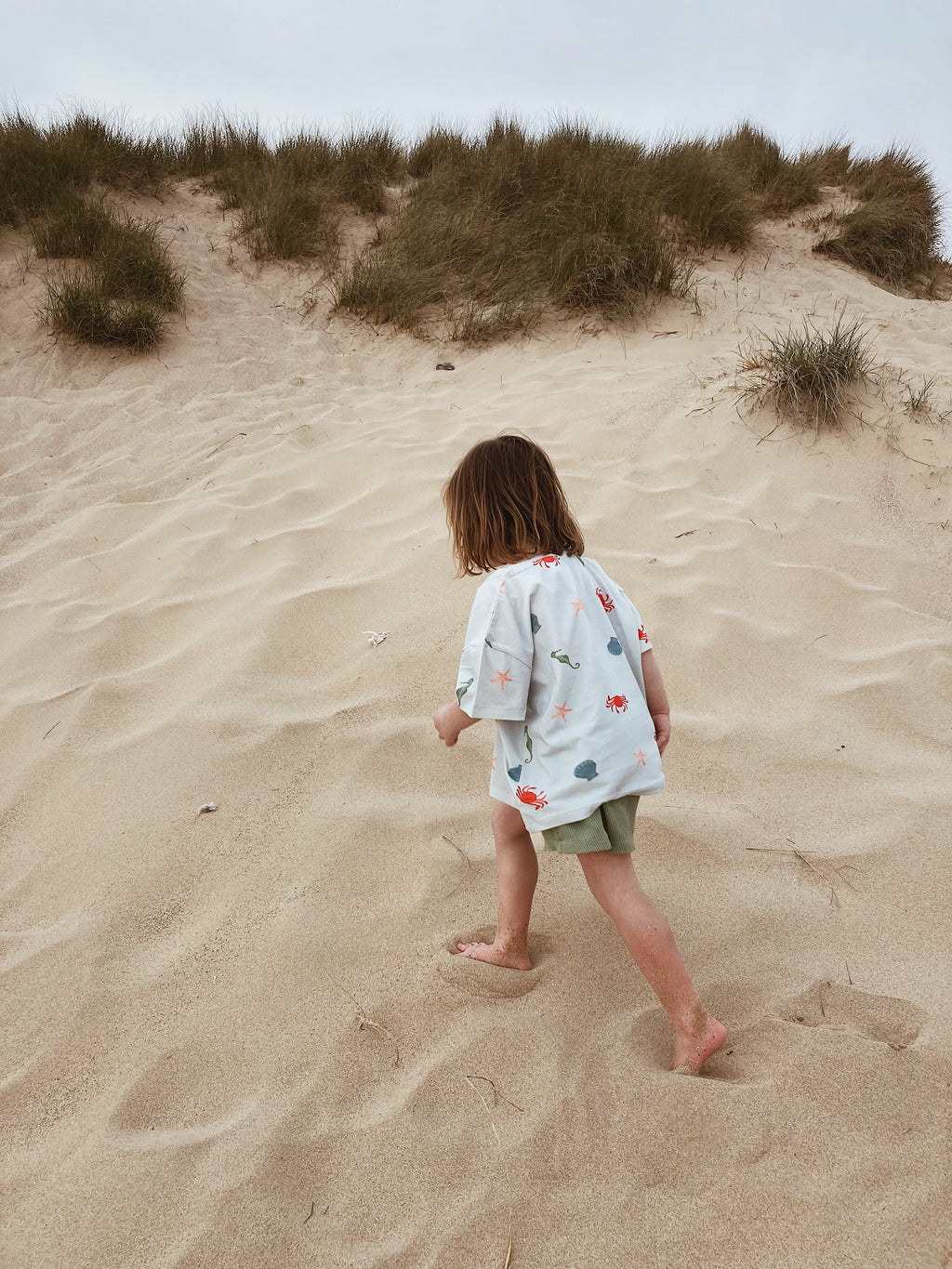 Child playing on a beach wearing Wildgreen organic cotton, gender-neutral marine t-shirt designed for sustainable, outdoor play.