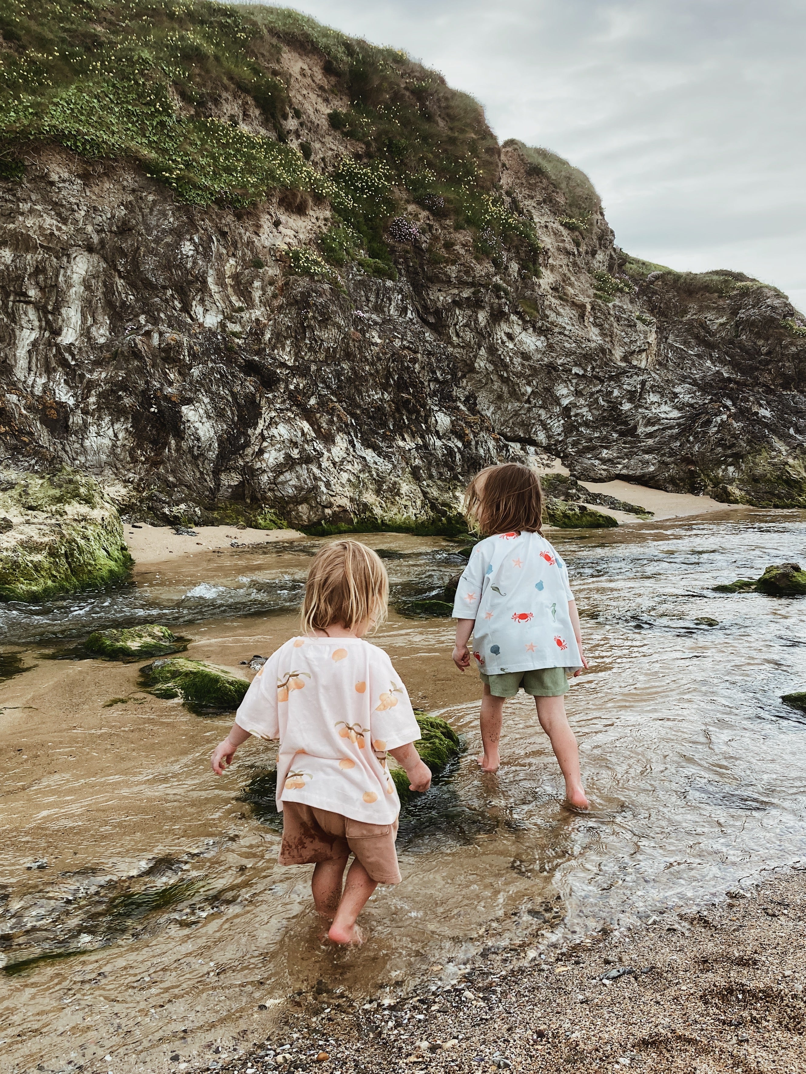 Two children playing in a beach river wearing Wildgreen organic cotton, gender-neutral t-shirts designed for sustainable, outdoor play.